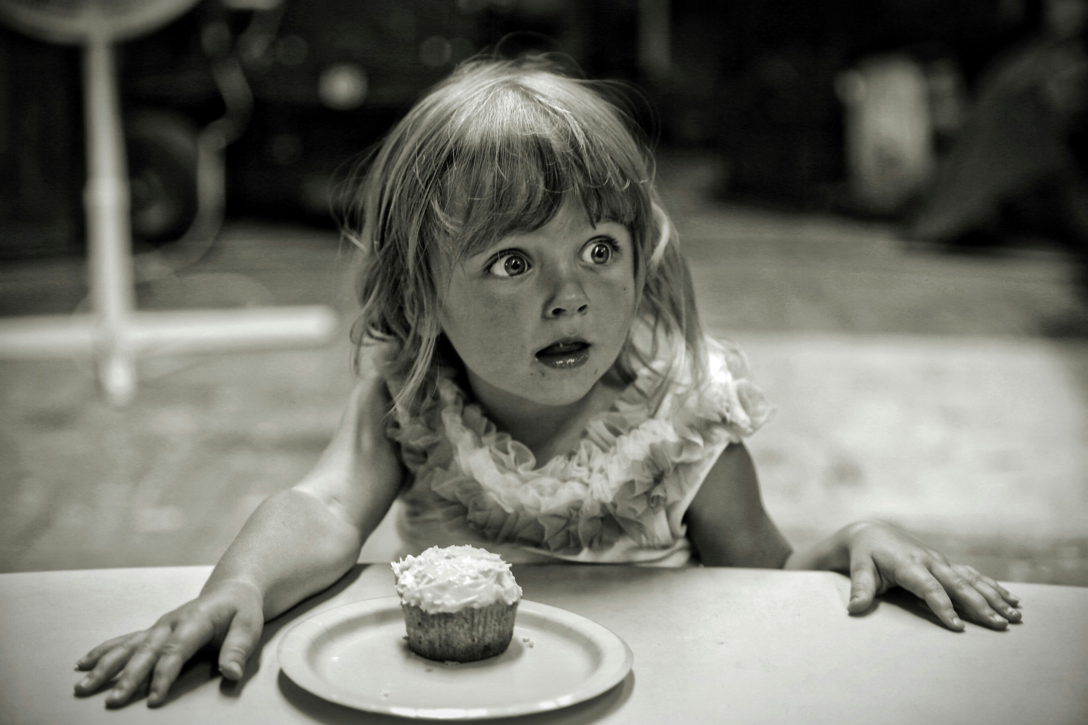 young girl looks surprised with a cupcake on a plate in front of her