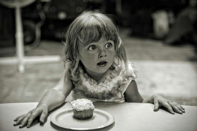 young girl looks surprised with a cupcake on a plate in front of her